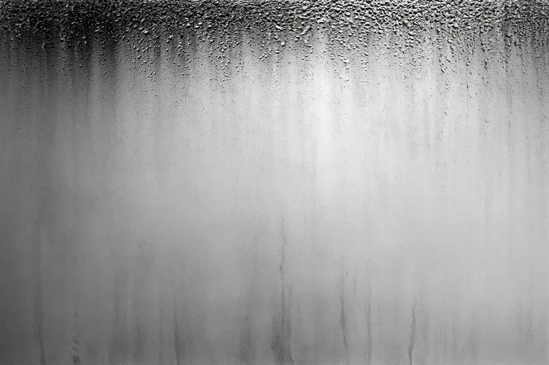 Condensation droplets and water streaks running down a fogged glass surface
