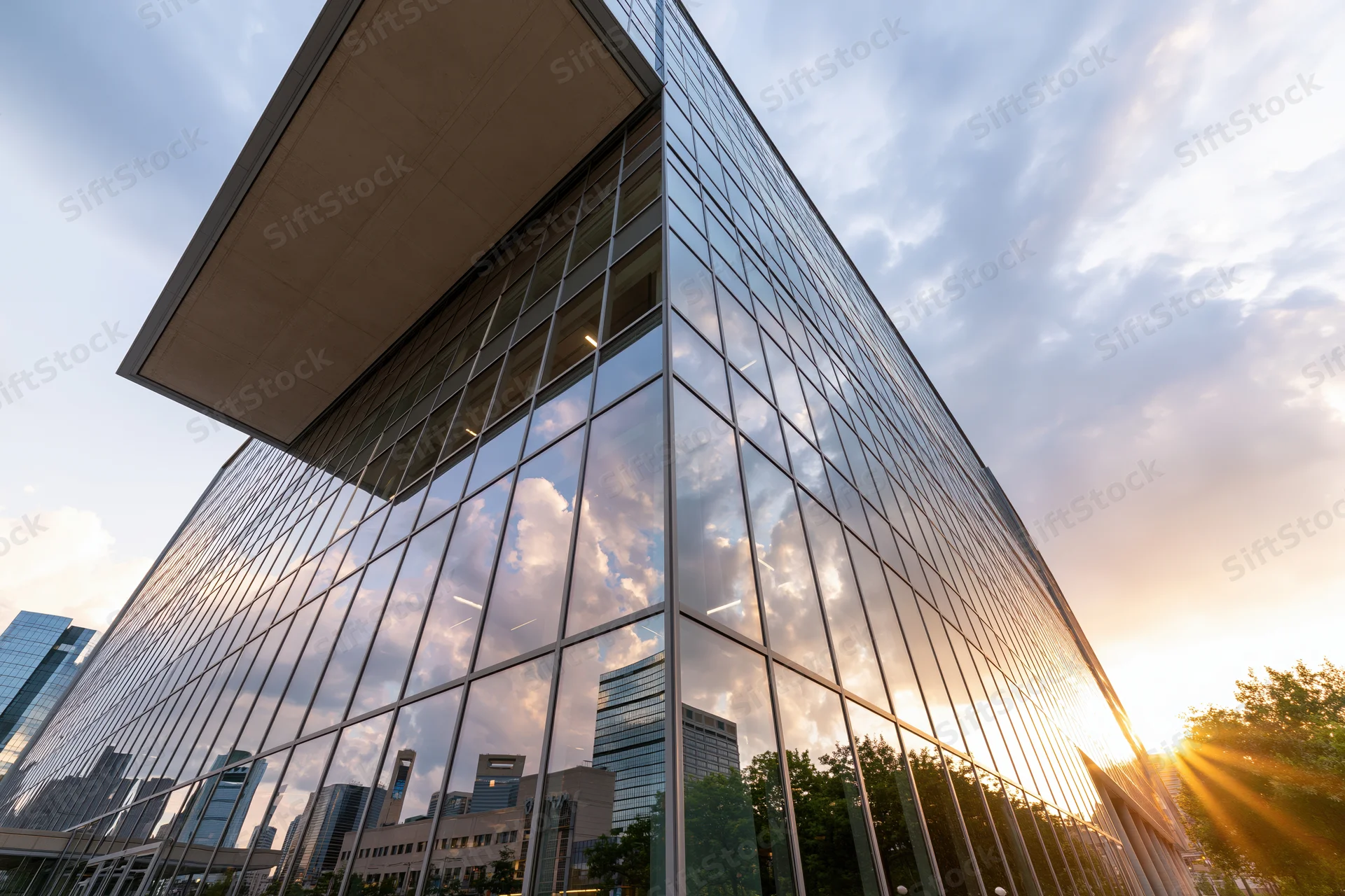 Corner of a modern glass-curtain-wall office building reflecting clouds and sunset in an urban setting