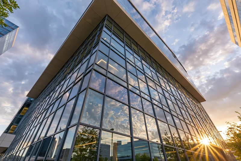 Corner of a modern glass-curtain-wall office building reflecting sunset sky and cityscape