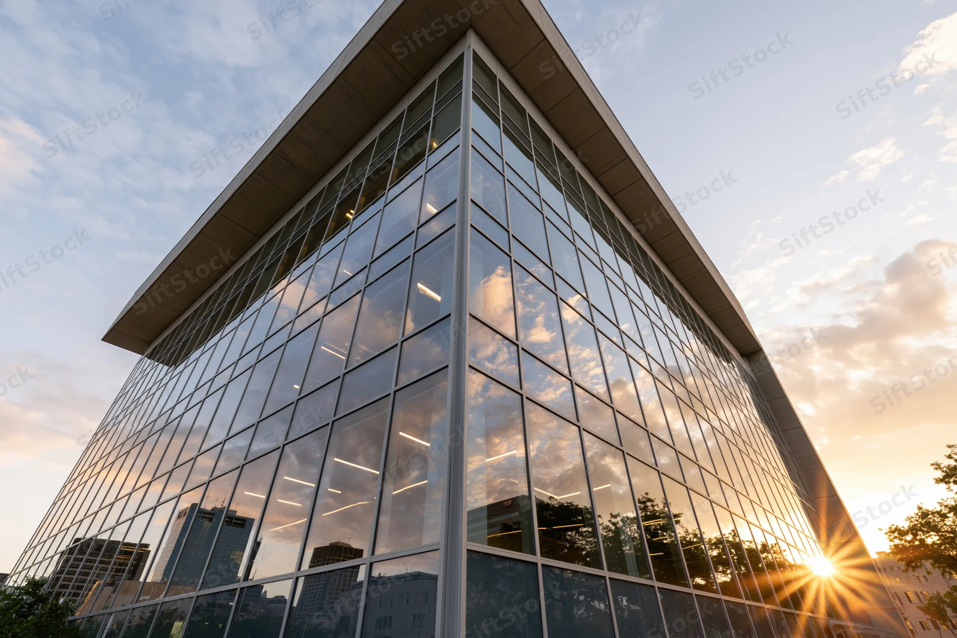 Corner of a modern glass-curtain-wall office building reflecting sunset sky and cityscape