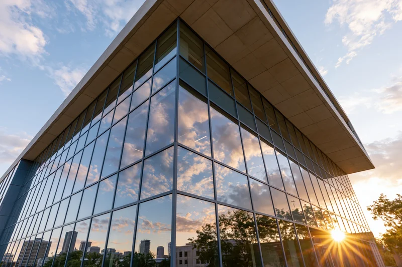 Corner of a modern glass-curtain-wall office building reflecting sunset sky and cityscape
