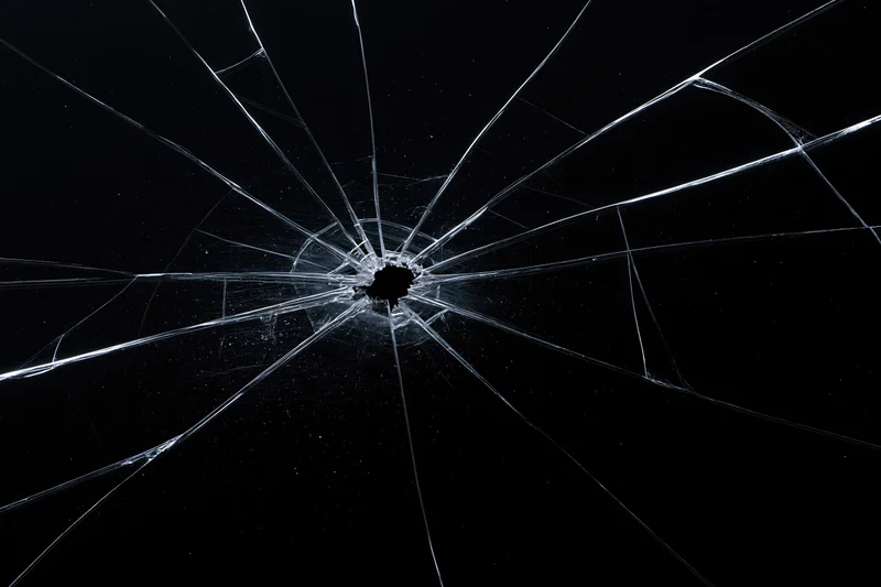 Cracked glass surface with a central impact point and radial fractures against a dark background