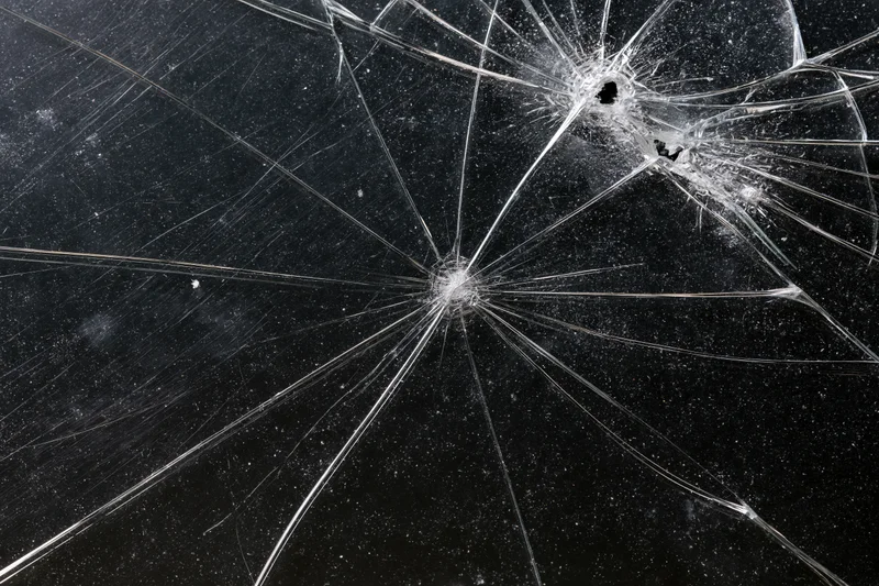 Cracked glass surface with radiating fracture lines spreading across dark background