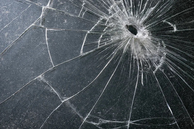 Cracked glass surface with radial fractures spreading from central impact hole