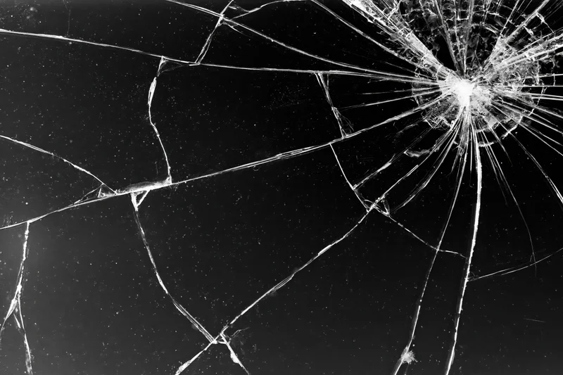 Cracked glass surface with radiating fracture lines spreading across dark background