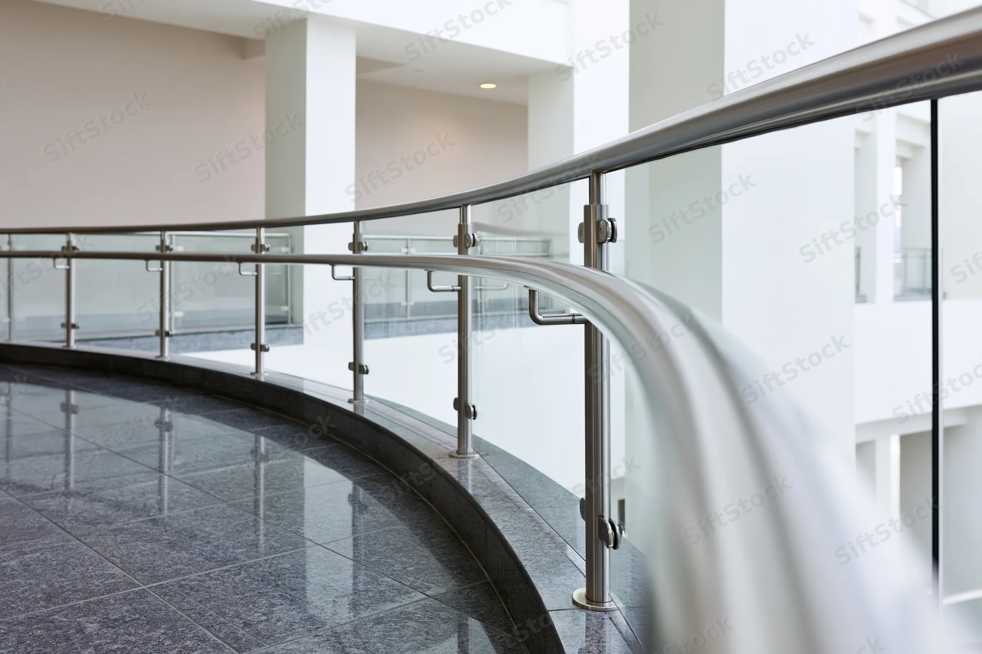 Curved glass and stainless steel balustrade railing along an interior hallway in a modern building