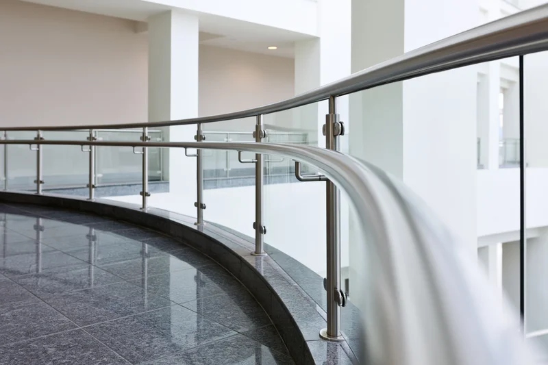Curved glass and stainless steel balustrade railing along an interior hallway in a modern building
