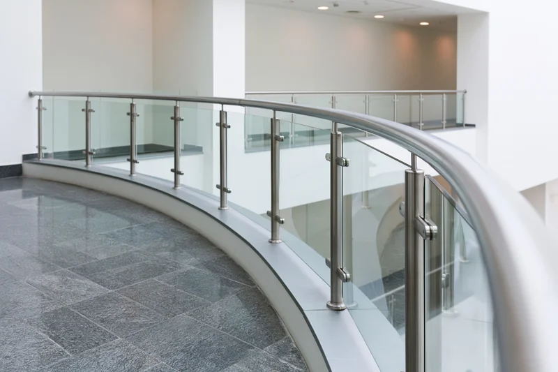Curved glass and stainless steel railing along an interior walkway in a modern building