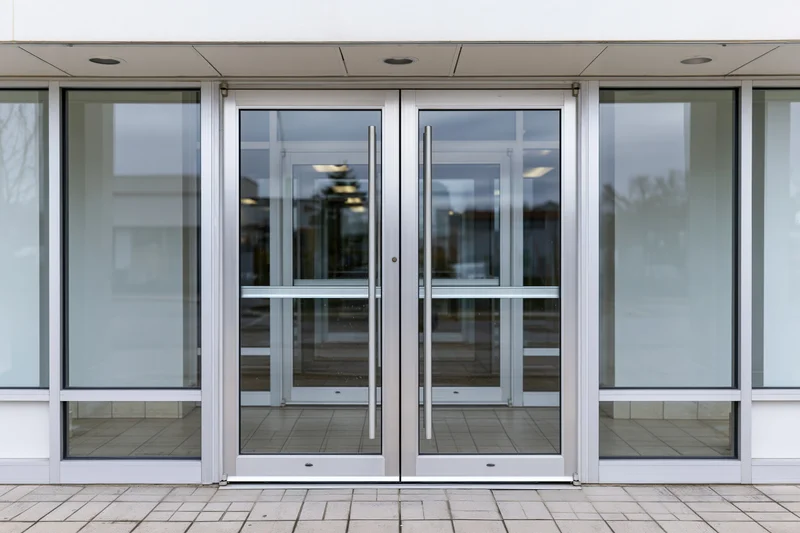 Double glass entrance doors with brushed aluminum frames and sidelights on a modern commercial building facade