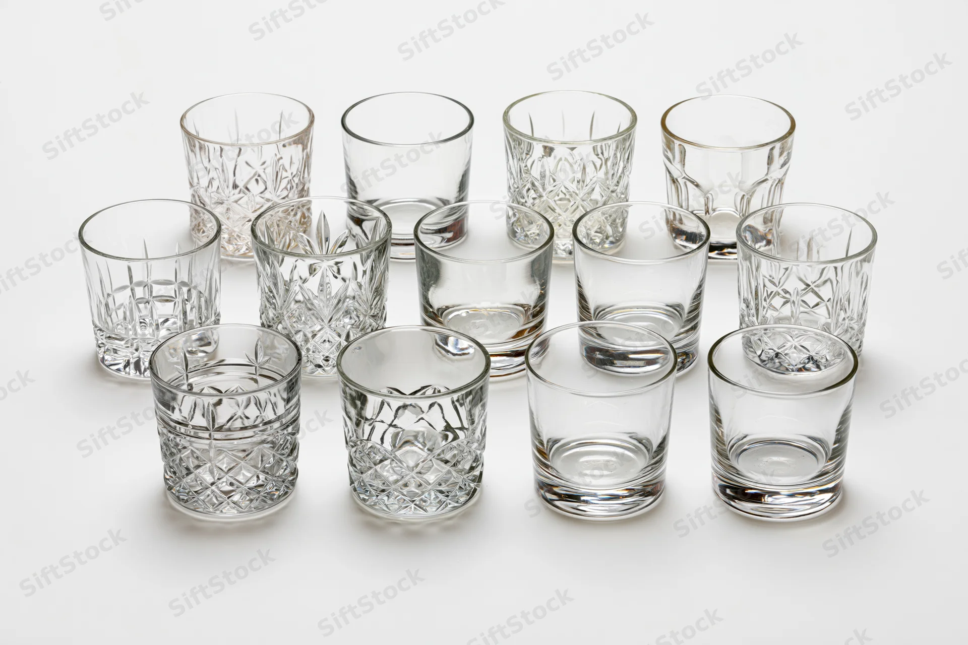Eighteen empty whiskey tumblers and rocks glasses arranged in rows on a white surface