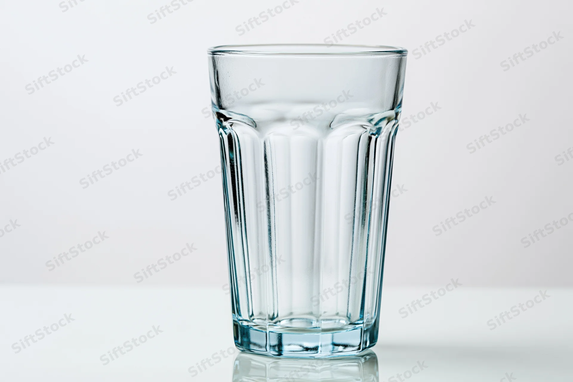 Empty faceted highball glass standing upright on a clean white surface with reflection