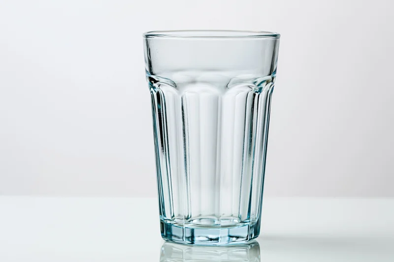 Empty faceted highball glass standing upright on a clean white surface with reflection