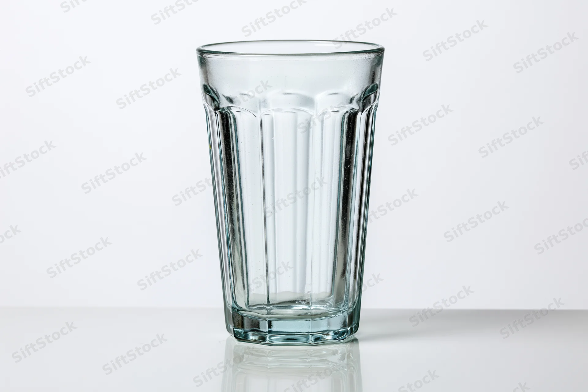 Empty faceted highball glass standing upright on a white reflective surface