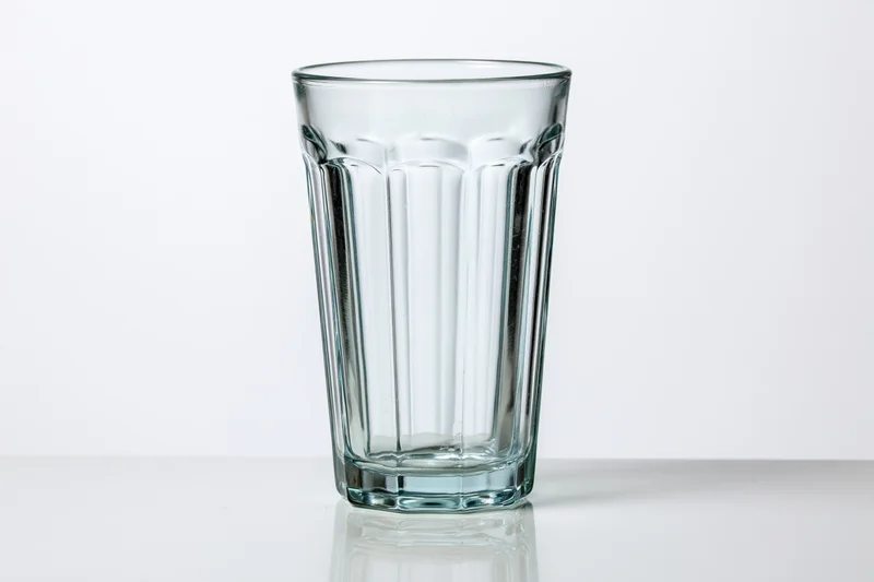 Empty faceted highball glass standing upright on a white reflective surface