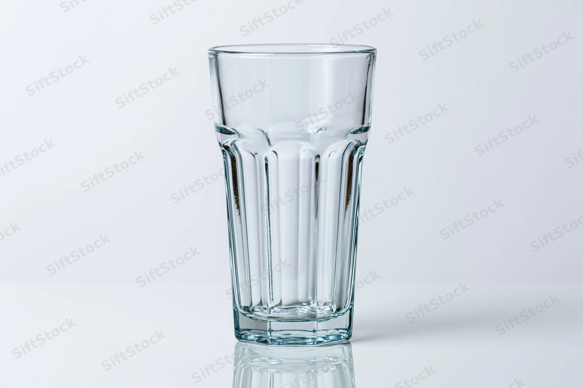 Empty faceted highball glass standing upright on a white reflective surface