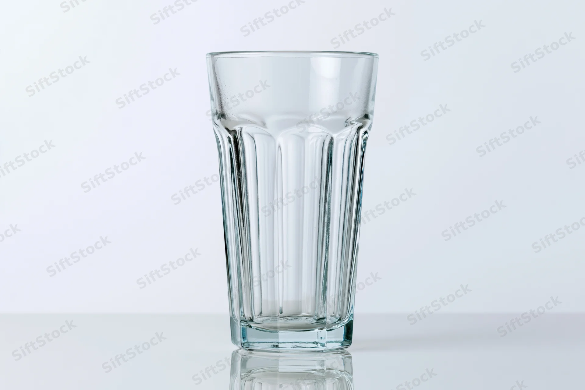 Empty faceted highball glass standing upright on a white surface with reflection and copyspace
