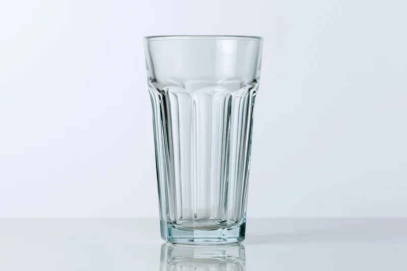 Empty faceted highball glass standing upright on a white surface with reflection and copyspace