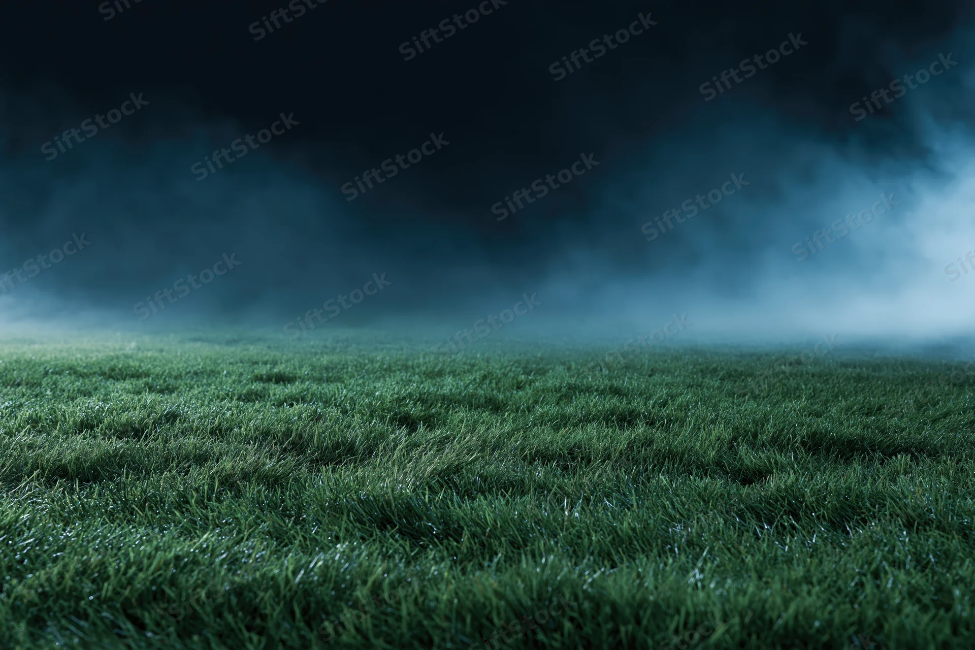 Low-angle view of a football pitch grass surface under dark misty sky