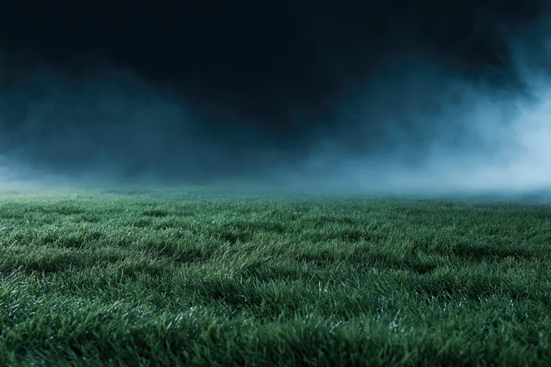 Low-angle view of a football pitch grass surface under dark misty sky