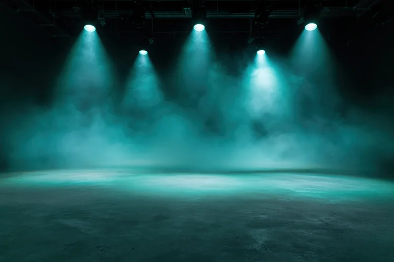 Empty stage floor illuminated by theatrical spotlights with teal light and smoke in a dark studio setting