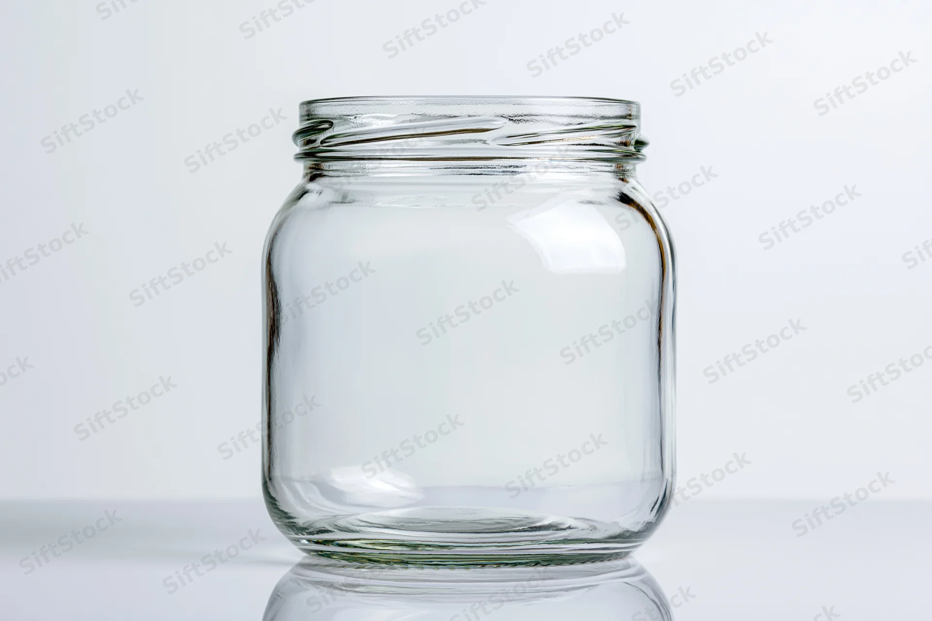 Empty wide-mouth glass jar sitting upright on a white reflective surface