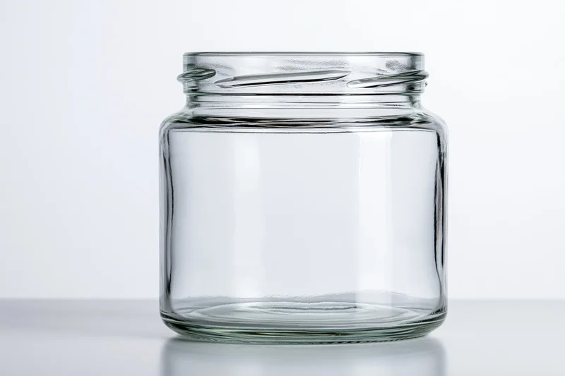 Empty wide-mouth glass jar sitting upright on a white surface