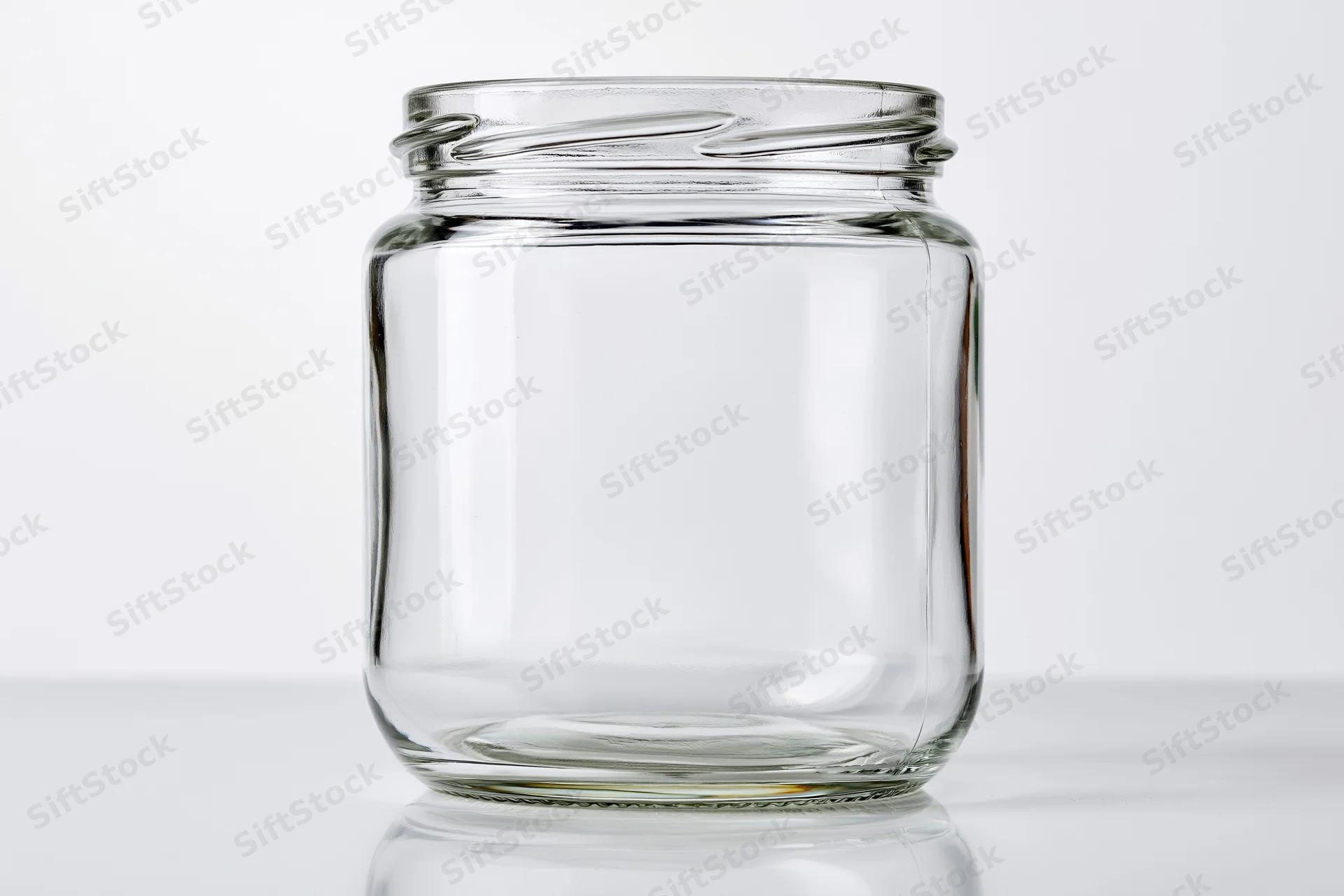 Empty wide-mouth glass jar sitting upright on a white reflective surface