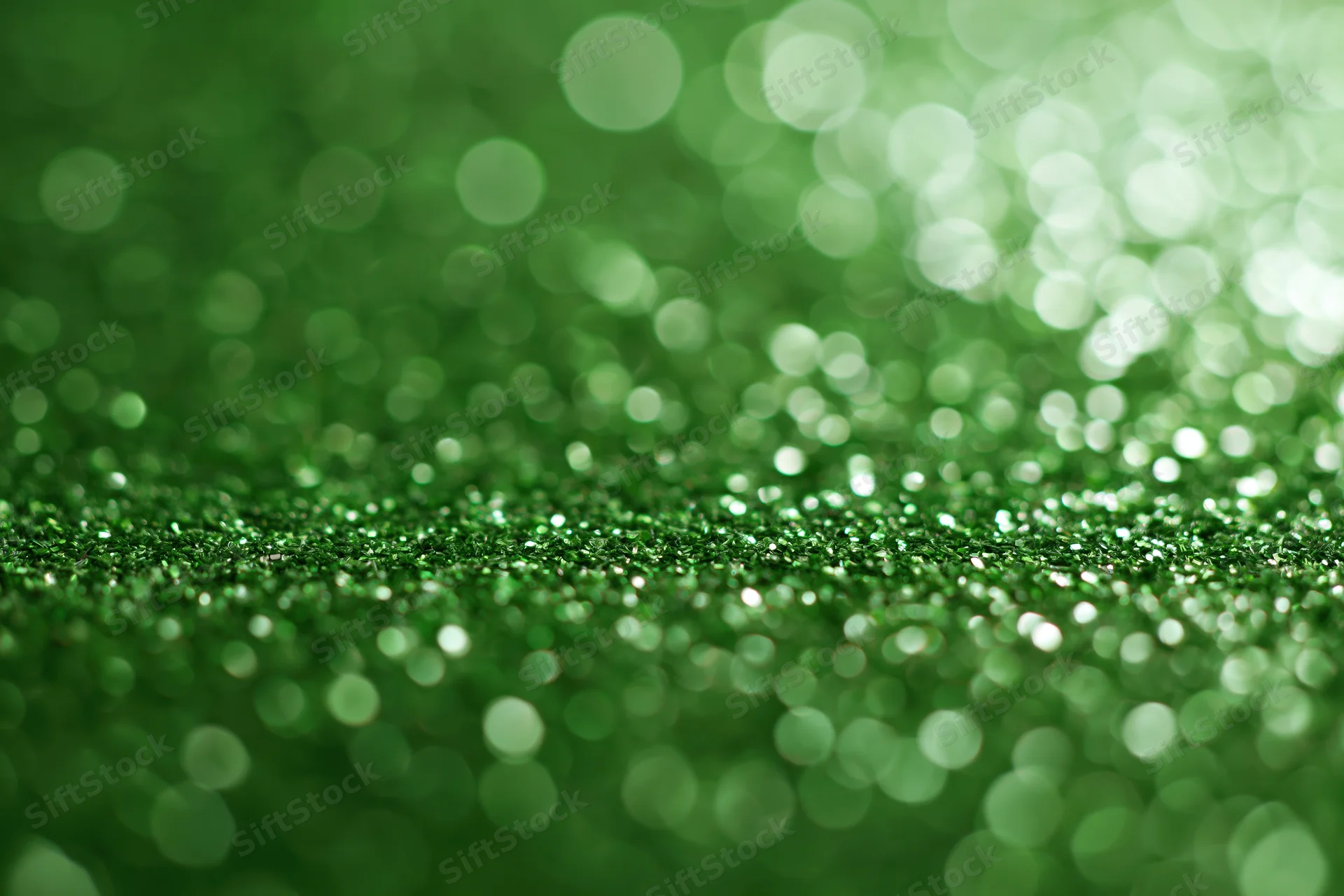Abstract green glitter background with bokeh lights and soft focus, featuring scattered sparkle and shimmer across the surface