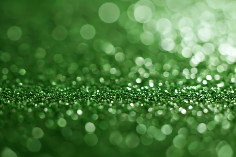 Abstract green glitter background with bokeh lights and soft focus, featuring scattered sparkle and shimmer across the surface