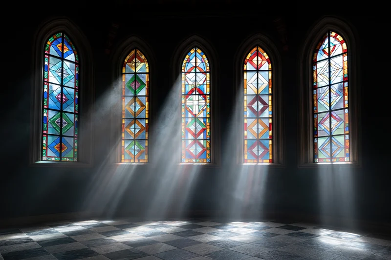 Five arched stained glass windows glowing with colored sunlight in a dark church interior