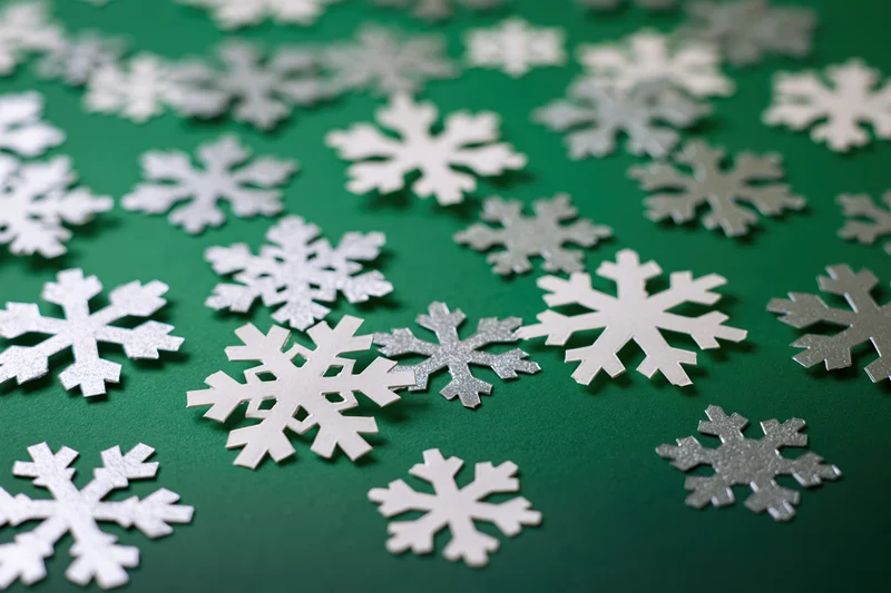 Scattered silver and white snowflake cutouts on a deep green holiday background