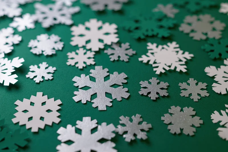 Silver and white paper snowflakes scattered across a deep green holiday background in a flat lay close-up