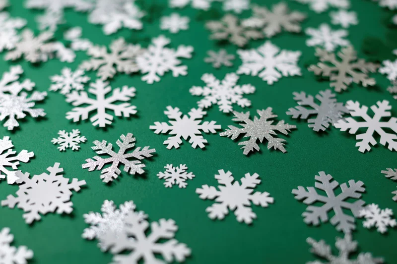 Scattered white and silver snowflake decorations on a deep green holiday background