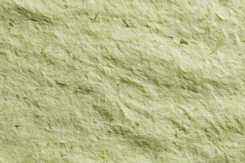 Close-up of a sheet of handmade recycled paper with visible fibers and green tint