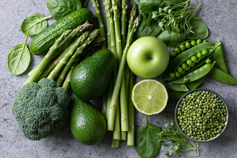 Flat lay of assorted green vegetables and fruits arranged on a gray stone countertop