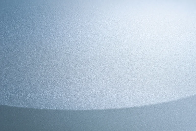 Frosted glass surface with smooth translucent texture filling the frame as a light blue gradient background