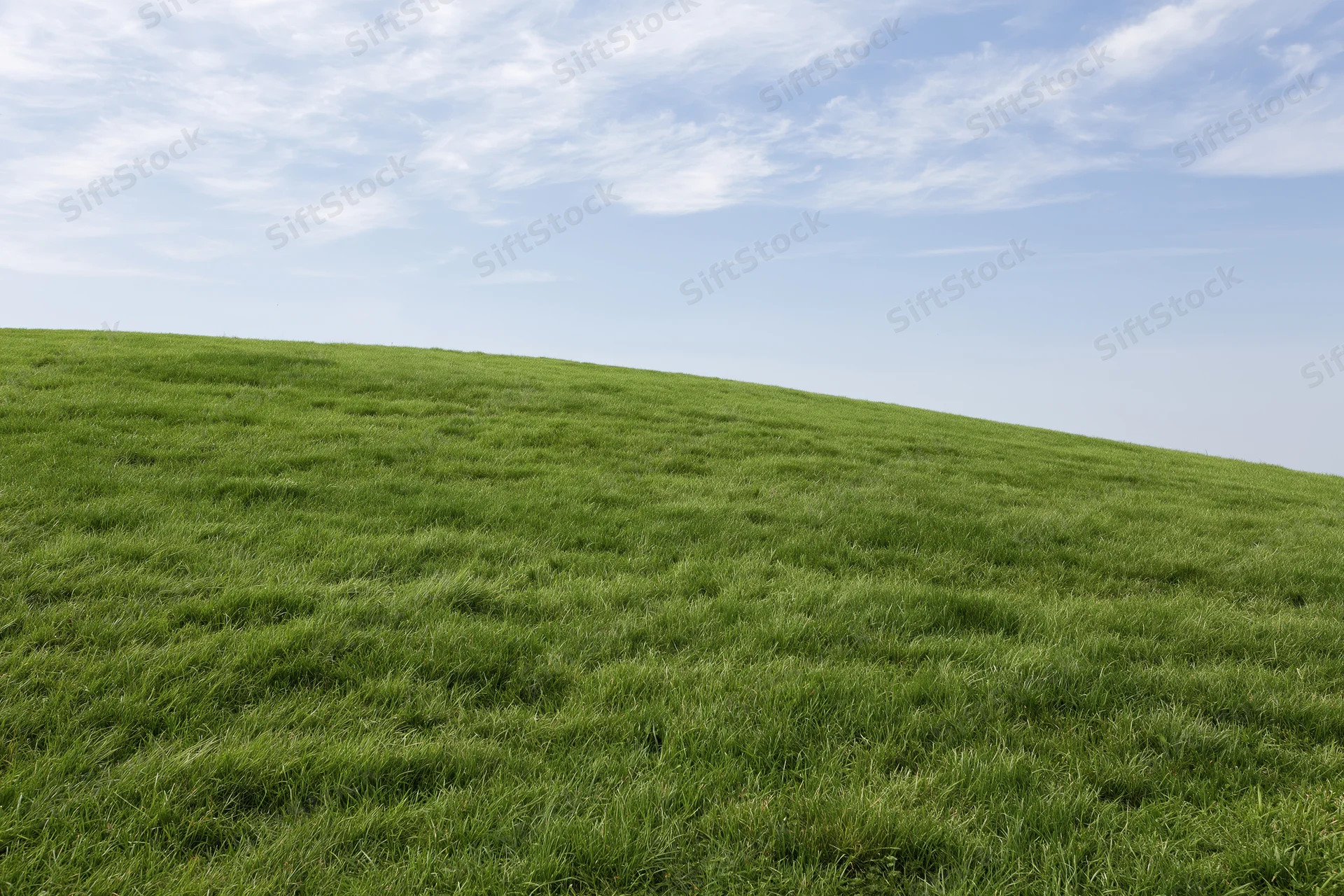 Gently rolling grass hill covered in short even green turf under a partly cloudy sky