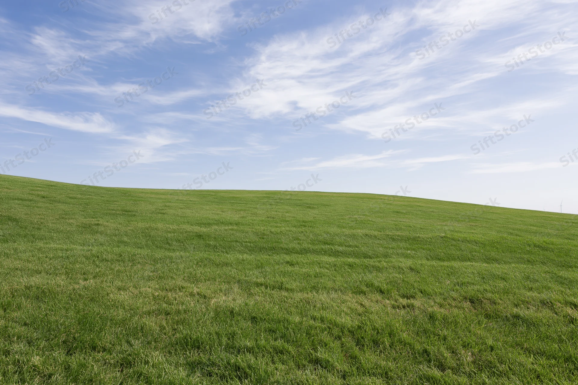 Gently rolling grass hill covered in short even green turf under a blue sky with wispy clouds