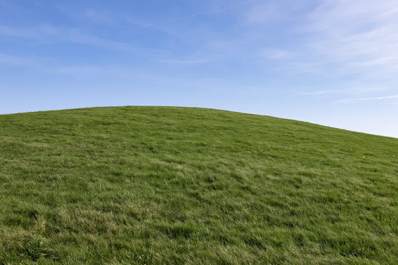 Gently sloping green grass hill rising to meet a clear blue sky