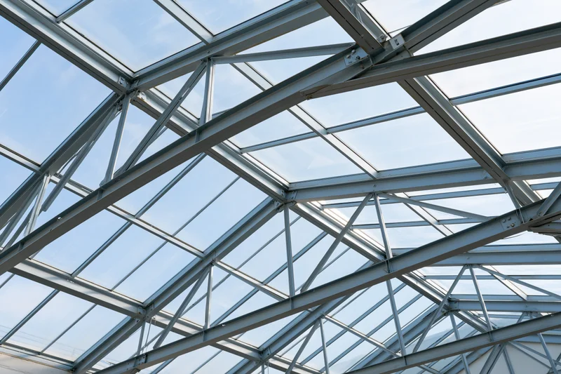 Geometric steel and glass roof structure viewed from below against a blue sky