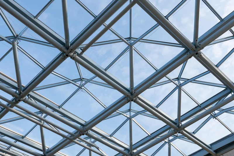 Geometric steel and glass roof structure viewed from below against a blue sky