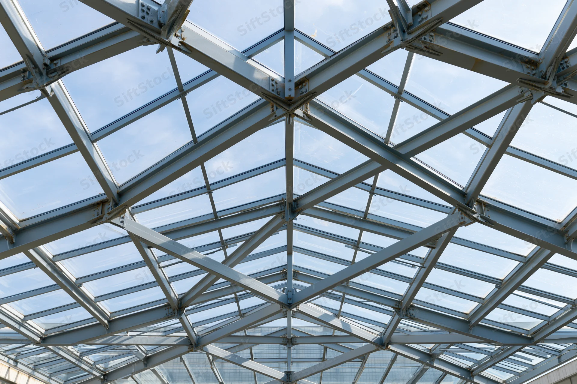 Geometric steel and glass roof structure viewed from below against a blue sky