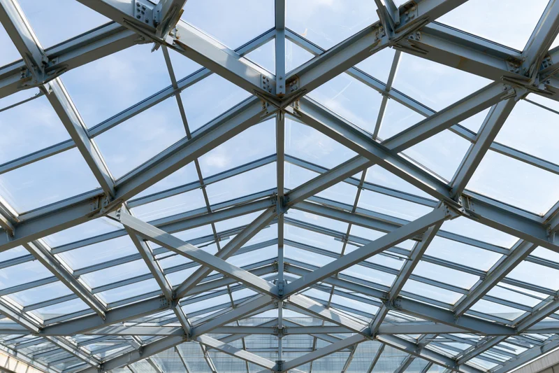 Geometric steel and glass roof structure viewed from below against a blue sky