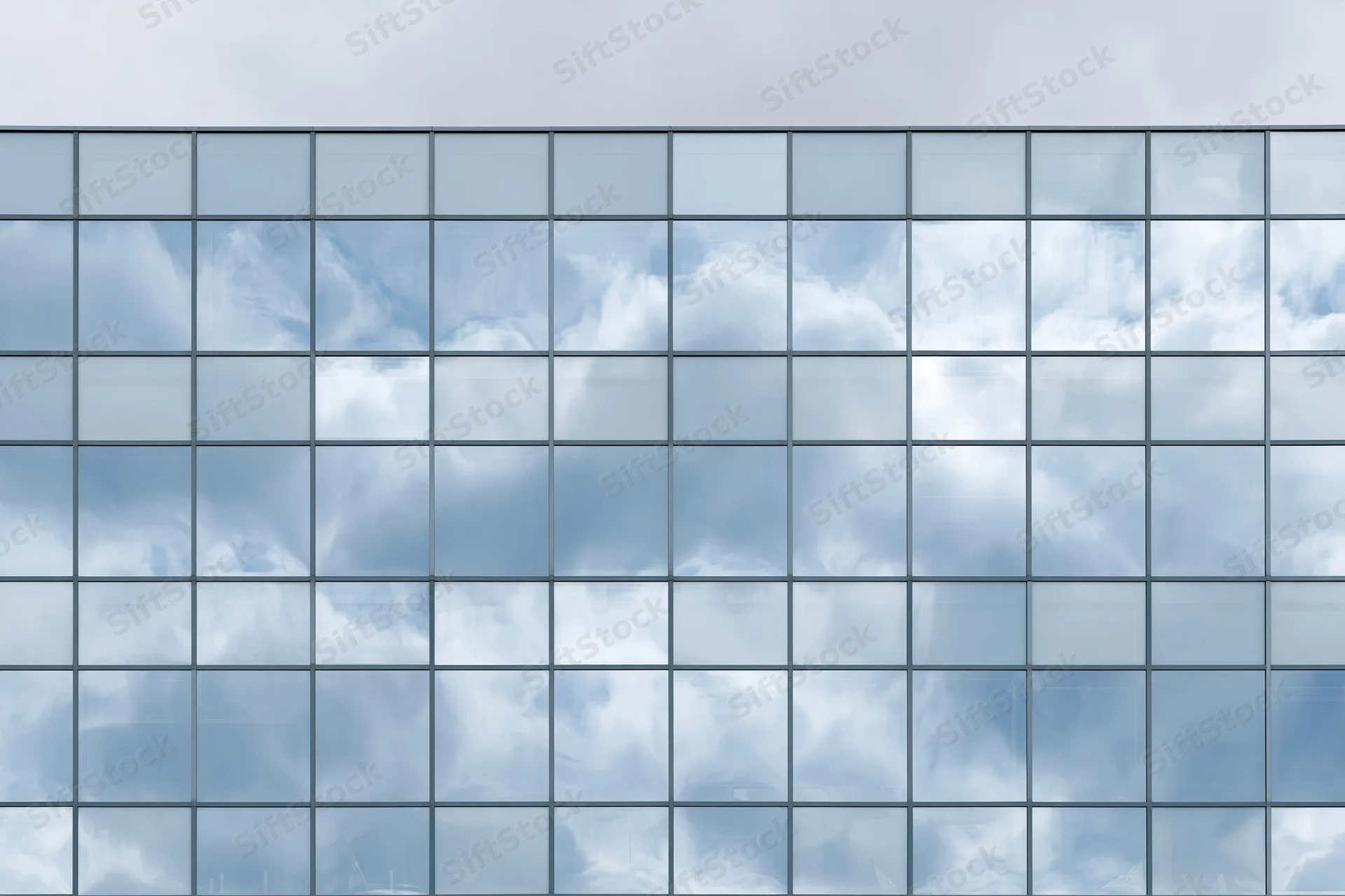 Glass curtain wall facade of a modern office building reflecting sky and clouds