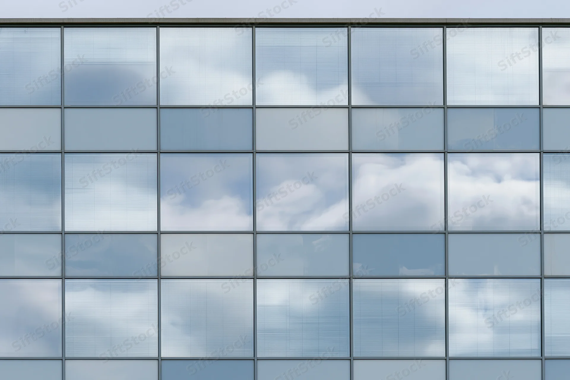 Glass curtain wall facade of a modern office building reflecting sky and clouds