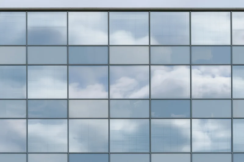 Glass curtain wall facade of a modern office building reflecting sky and clouds