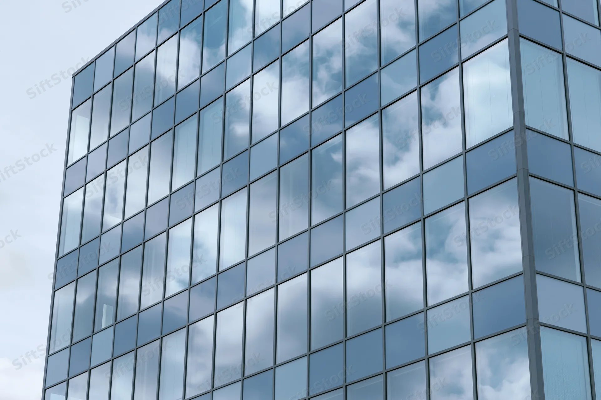 Glass curtain wall facade of a modern office building reflecting sky and clouds