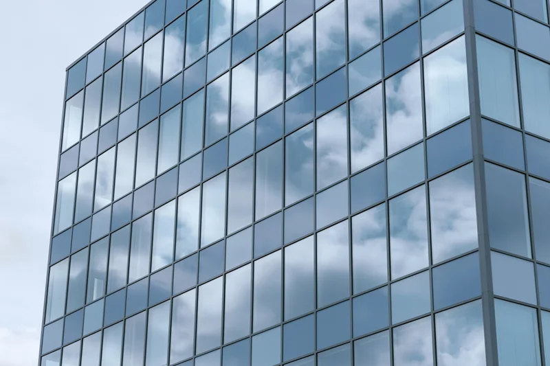 Glass curtain wall facade of a modern office building reflecting sky and clouds