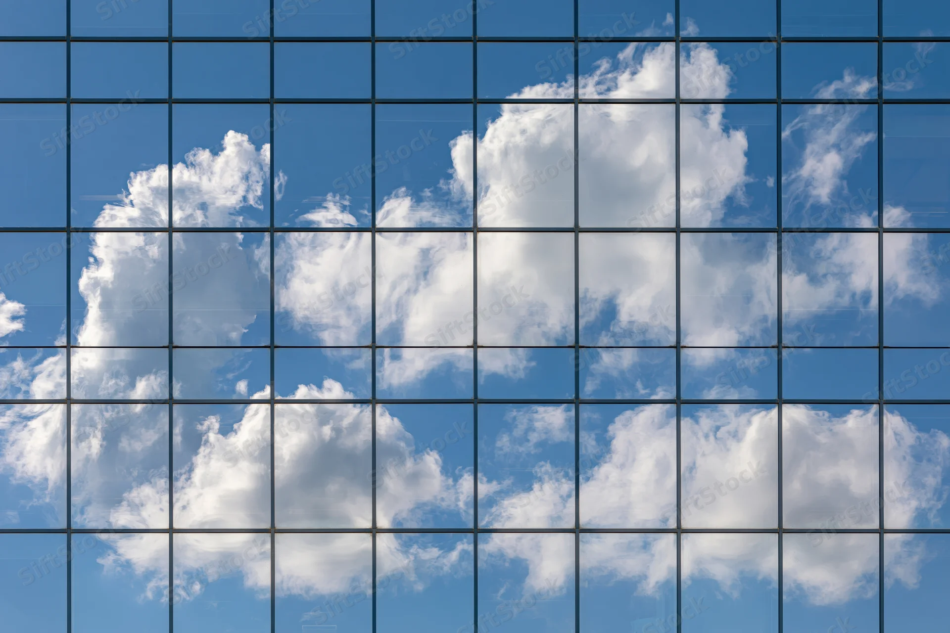 Glass curtain wall of a modern office building reflecting blue sky and white clouds