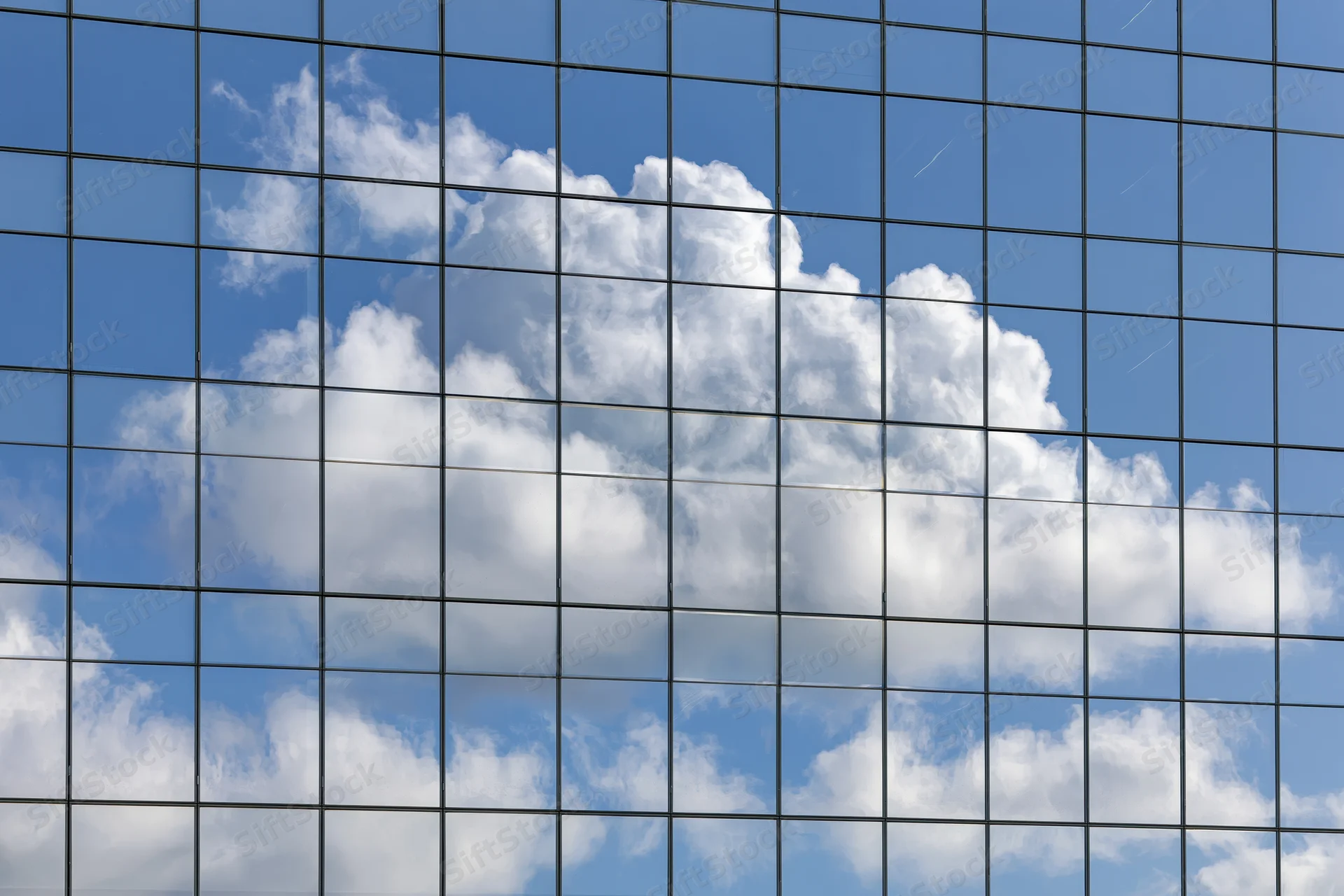 Glass curtain wall of a modern office building reflecting blue sky and white clouds